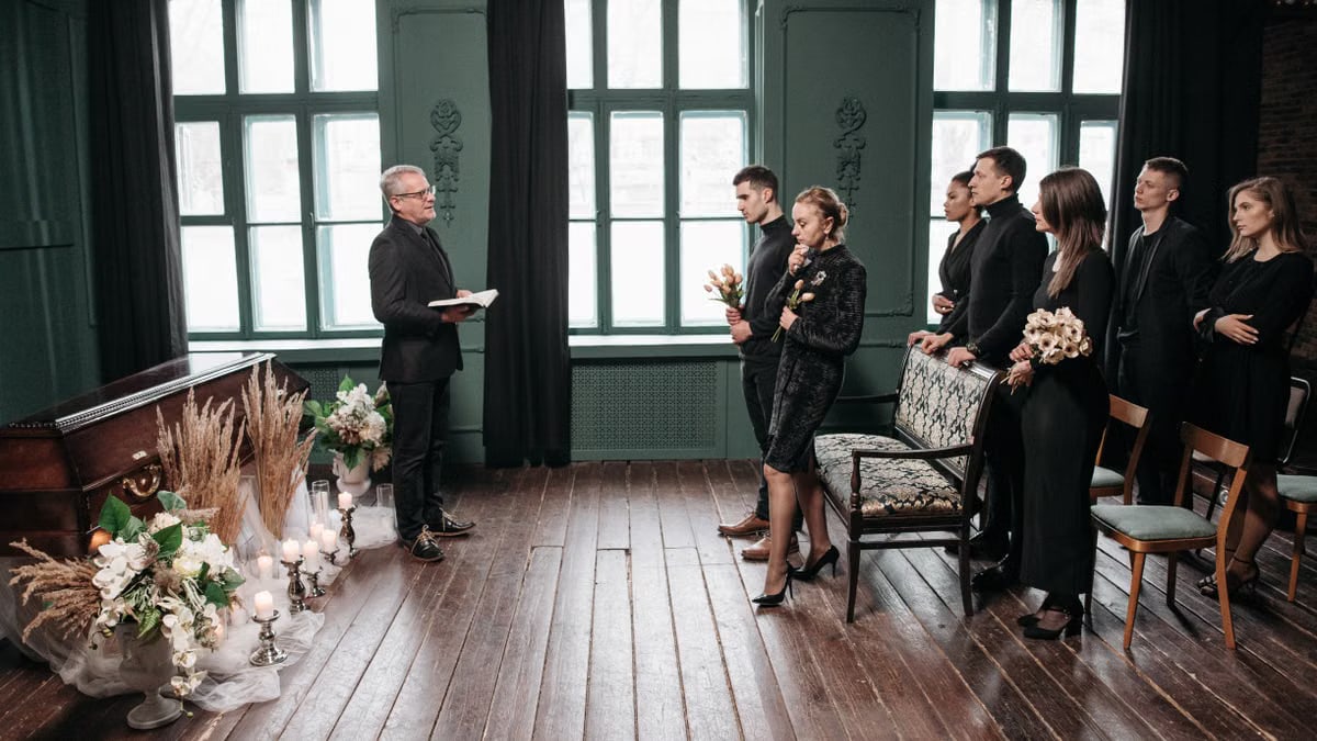 A somber indoor funeral service with people gathered around a coffin, expressing sorrow.